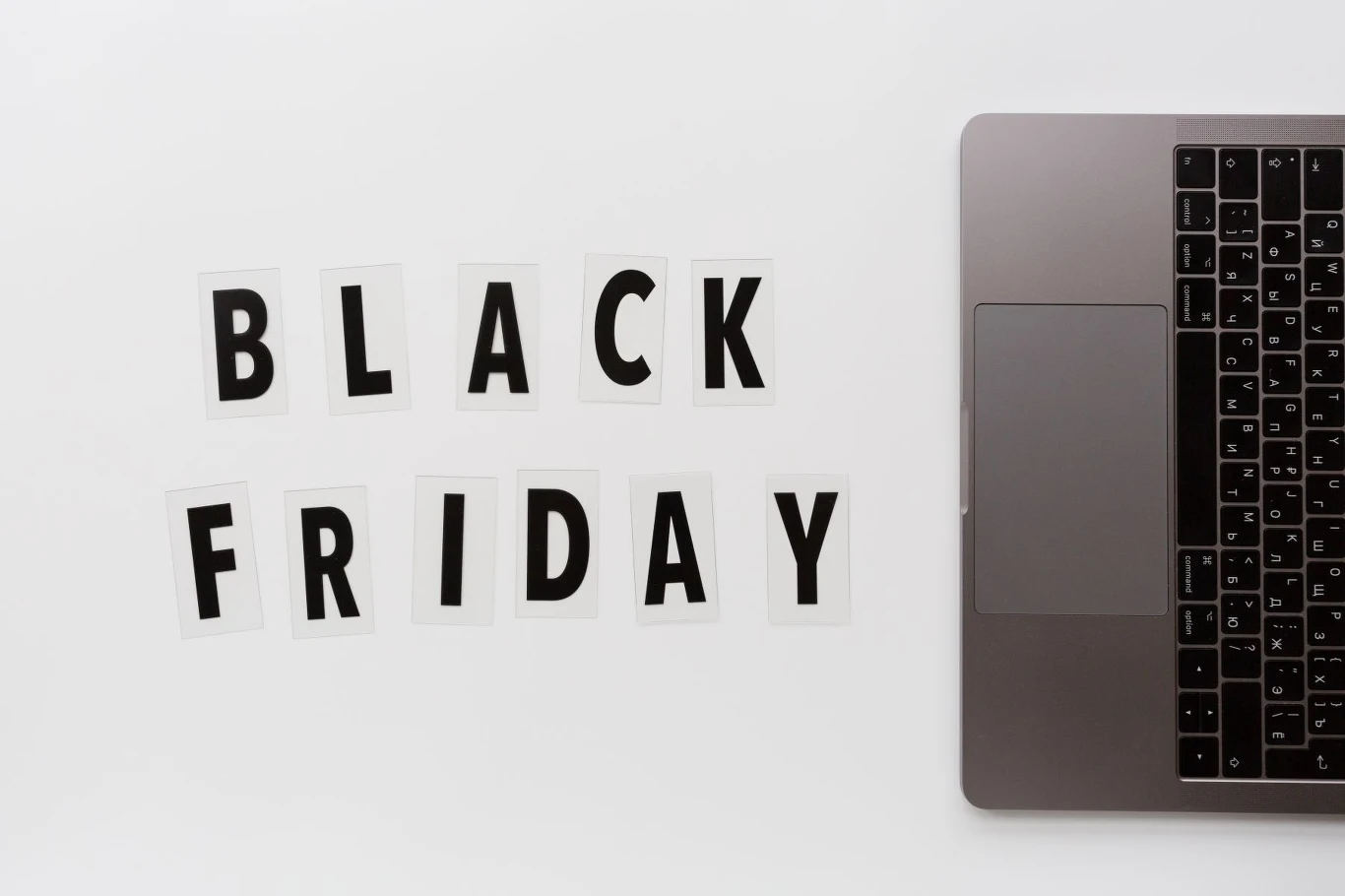 Black Weeks w Media Expert Napis „BLACK FRIDAY” ułożony z czarnych liter na białych kartkach obok fragmentu otwartego laptopa na białym tle.