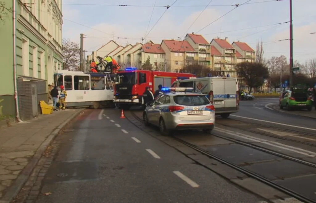 Wypadek tramwaju na ul. Parkowej w Szczecinie Strażacy i służby ratunkowe pracują przy tramwaju, który zderzył się z budynkiem na skrzyżowaniu, w tle budynki mieszkalne i zaparkowane pojazdy służbowe, utrudniony przejazd na ulicy.