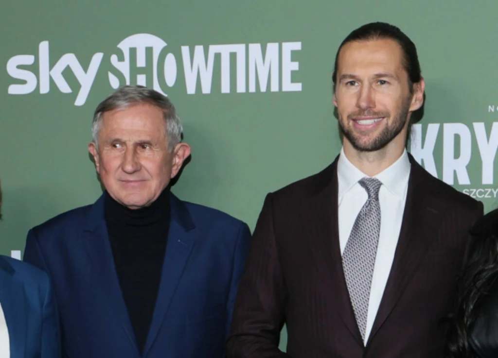 Edward Krychowiak, ojciec Grzegorza i Grzegorz Krychowiak Dwóch mężczyzn ubranych elegancko, starszy w granatowej marynarce i czarnym golfie, młodszy w garniturze i krawacie, stoją na tle zielonej ścianki z logotypami Sky Showtime.