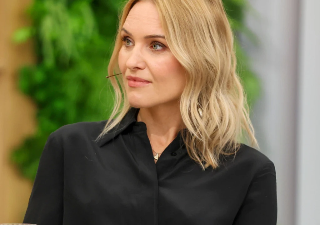 Magdalena Chorzewska - była ekspertka "Ślubu od pierwszego wejrzenia" Kobieta o blond włosach ubrana w czarną koszulę siedzi w jasnym pomieszczeniu, w tle zielona roślinność rozmieszczona na ścianie.