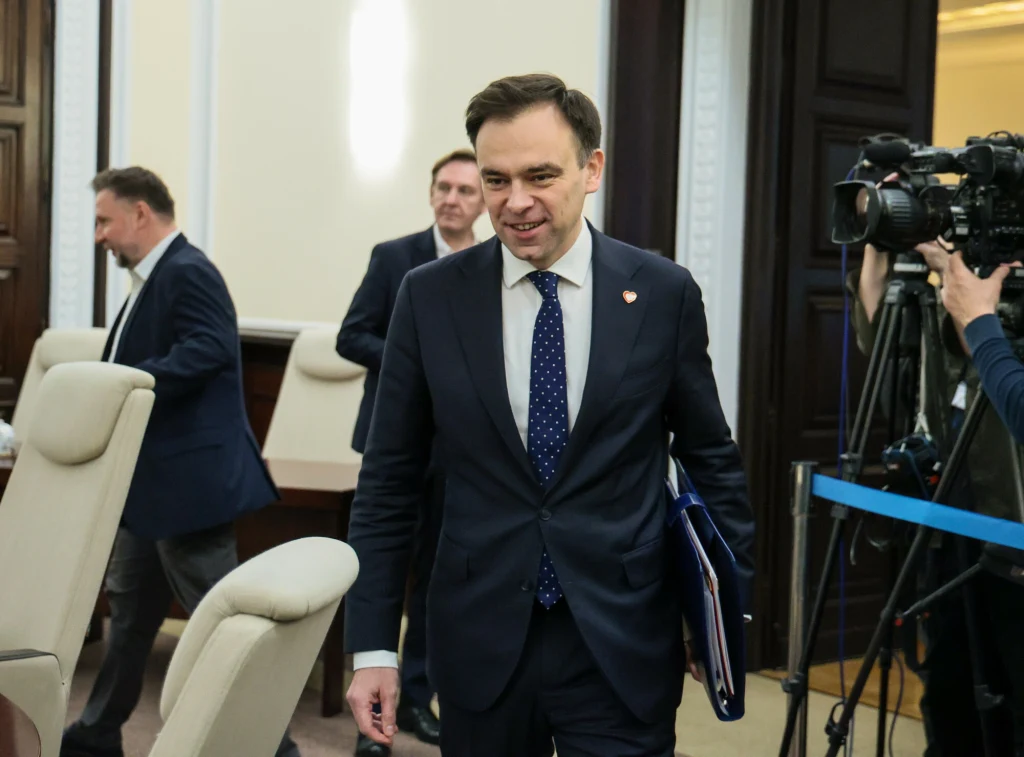 Ustawa okołobudżetowa w Senacie bez poprawek (zdj. ilustracyjne) Mężczyzna w garniturze z teczką w ręku wchodzi do sali konferencyjnej, w tle kilku innych mężczyzn oraz ekipa kamerzystów rejestrująca wydarzenie.