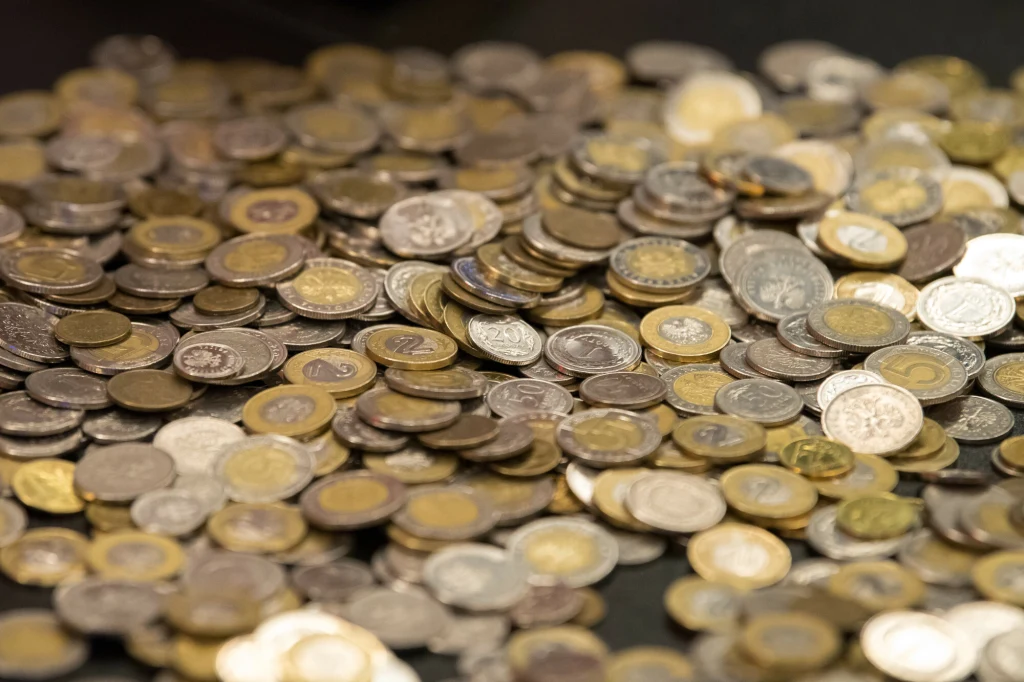 Stosy rozsypanych monet różnych nominałów i kolorów leżących na czarnym tle, dominują monety z wyraźnymi detalami wybitymi na powierzchni.