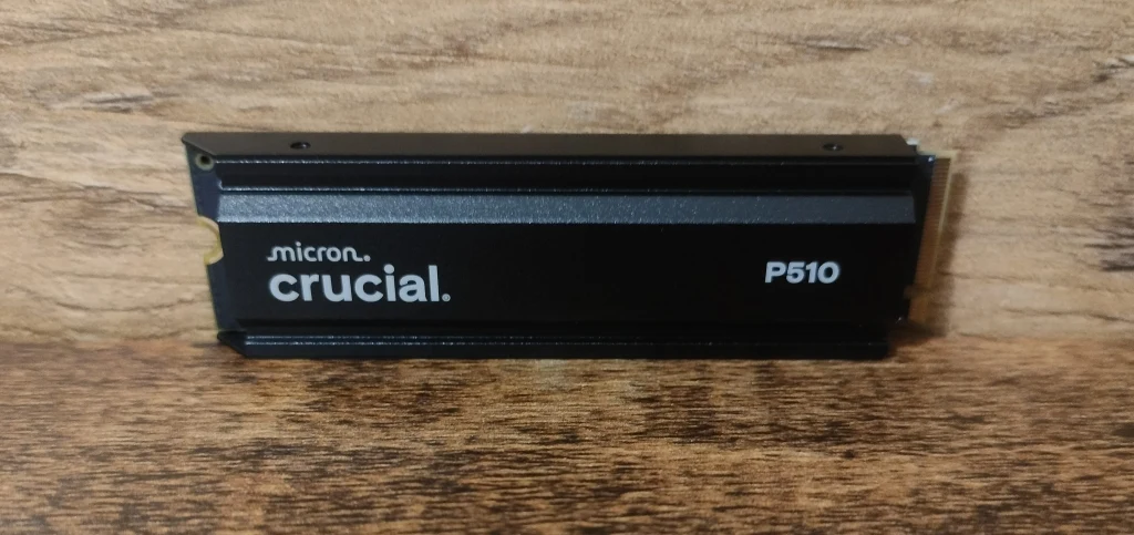 Crucial P510 Czarny dysk SSD Micron Crucial P510 z wyraźnym logo producenta, umieszczony na tle drewnianej powierzchni.