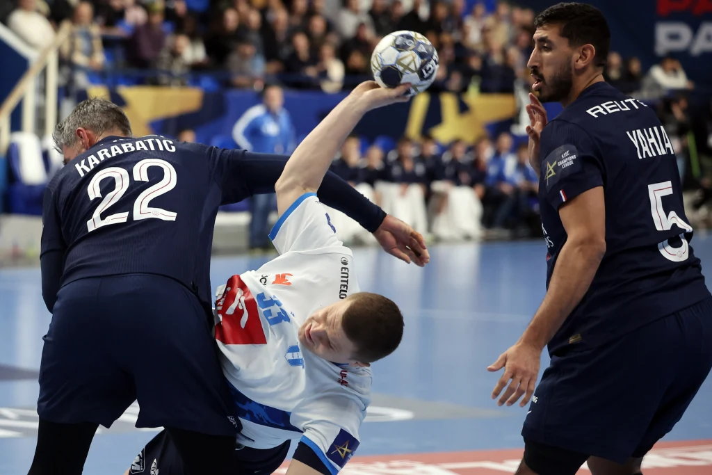 Dynamiczna walka podczas meczu piłki ręcznej, trzech zawodników ściera się o piłkę, jeden z nich próbuje utrzymać równowagę podczas kontaktu z przeciwnikami.