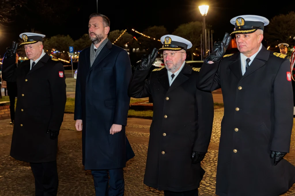 Kosiniak-Kamysz o zakupie okrętów podwodnych. "Na to czekały pokolenia marynarzy" Czterech mężczyzn w mundurach marynarki wojennej oraz w eleganckim płaszczu stoi w szeregu podczas oficjalnej uroczystości nocą. Trzech mężczyzn w mundurach wykonuje salut, a w tle widoczne są oświetlone lampy i elementy dekoracyjne.