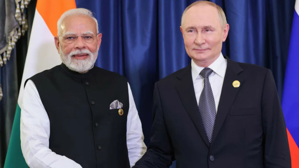 Narendra Modi i Władimir Putin. Prezydent Rosji odwiedzi Indie Dwóch mężczyzn w eleganckich garniturach podaje sobie dłonie na tle flag Indii i Rosji.