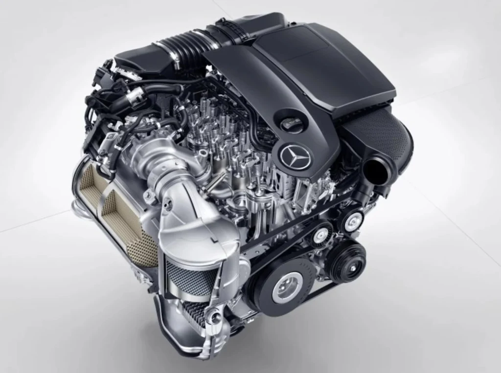 Silnik Mercedes OM654 imponuje niskim zużyciem paliwa i wysoką kulturą pracy Nowoczesny silnik samochodowy marki Mercedes-Benz z widocznym logo na pokrywie, charakteryzujący się licznymi podzespołami mechanicznymi, rurami i elementami sterującymi, przedstawiony na jasnym tle.