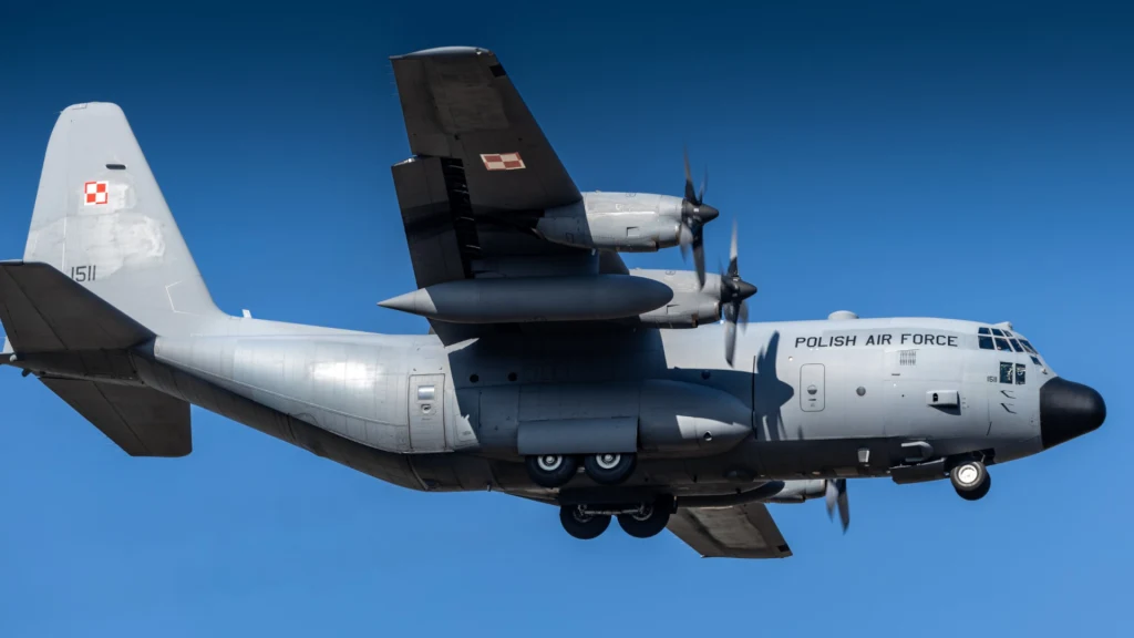 Transportowy samolot wojskowy z napisem Polish Air Force oraz oznaczeniem Sił Powietrznych RP na jasnoszarym kadłubie, lecący na tle bezchmurnego, niebieskiego nieba, widoczne dwa silniki oraz detale konstrukcyjne.