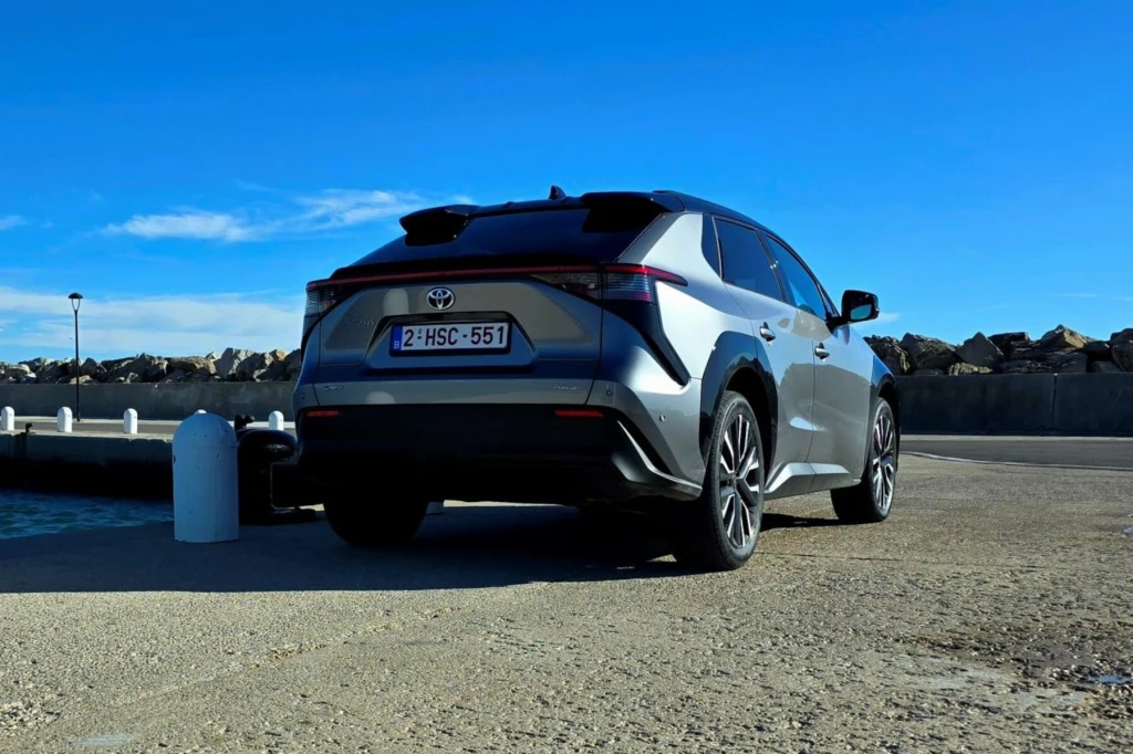 Nowoczesny samochód marki Toyota stoi zaparkowany na betonowej powierzchni przy nabrzeżu portowym, w tle widoczny jest falochron oraz niebieskie niebo z delikatnymi chmurami.