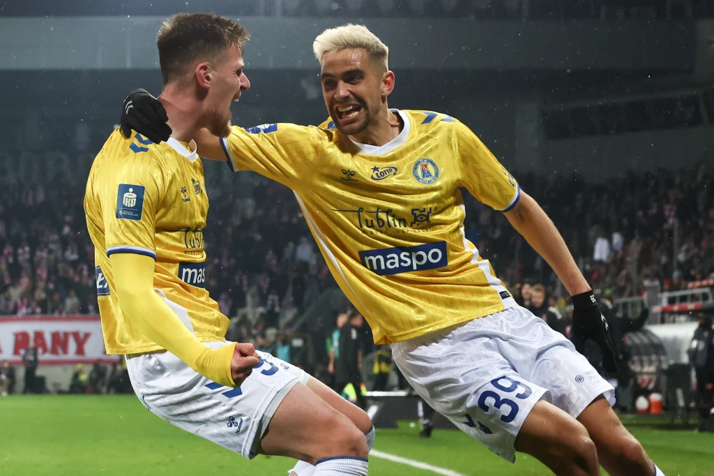 Dwaj piłkarze drużyny w żółtych koszulkach celebrują zdobycie bramki na stadionie pełnym kibiców, wyrażając radość i sportowe emocje.