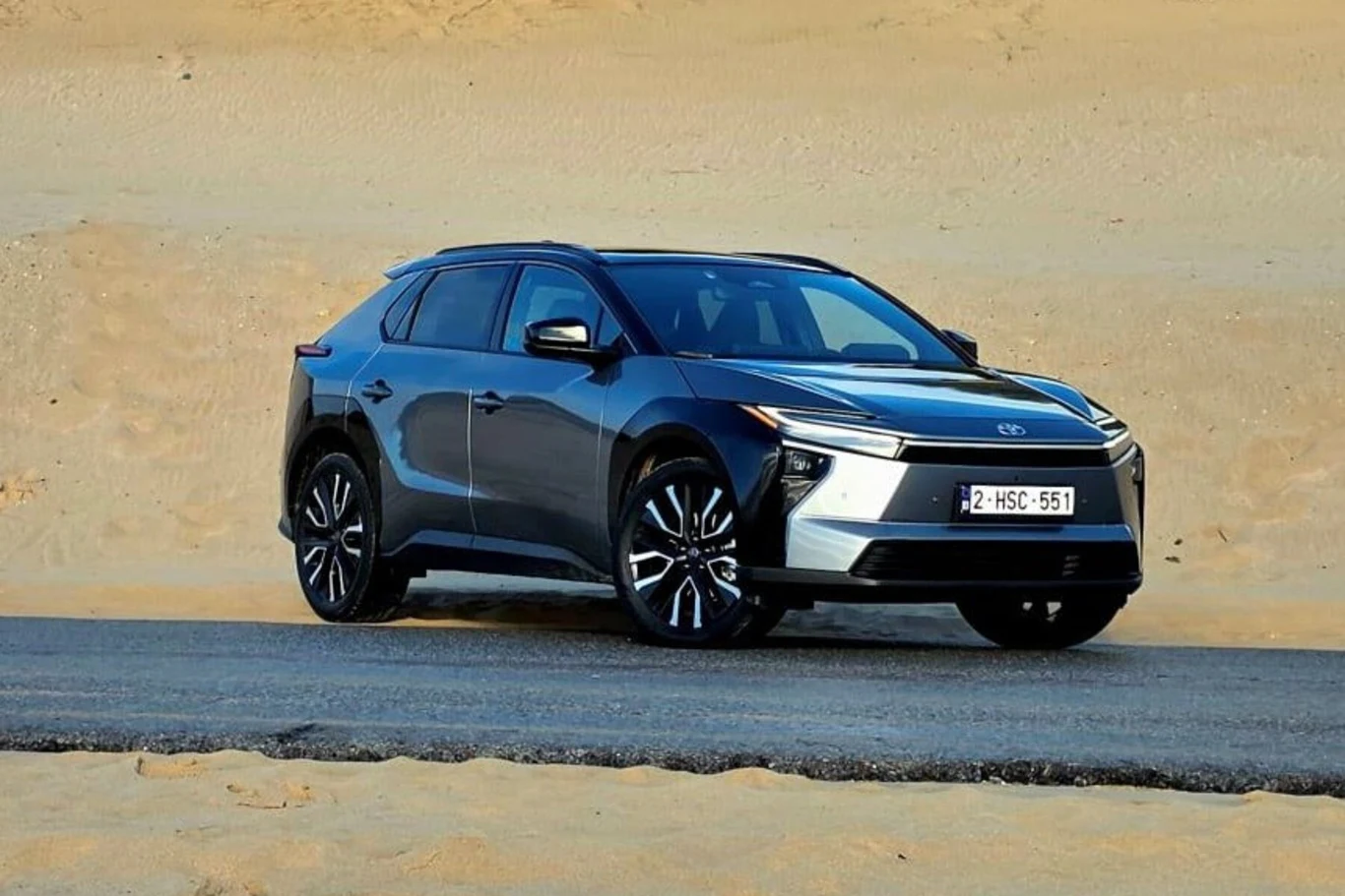 Nowoczesny, czarny SUV z charakterystycznym wzorem przednich świateł stoi zaparkowany na asfalcie przy pustynnym terenie, auto posiada belgijskie tablice rejestracyjne.