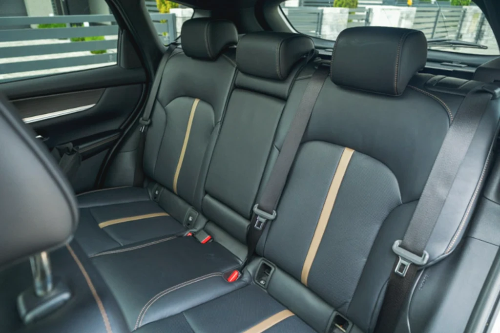 Ilość miejsca na tylnej kanapie CX-60 nie jest mała, ale od tak dużego SUV-a należałoby oczekiwać więcej Czarne, skórzane tylne siedzenia samochodu z pionowymi, jasnobrązowymi paskami ozdobnymi, widoczne trzy zagłówki i trzypunktowe pasy bezpieczeństwa