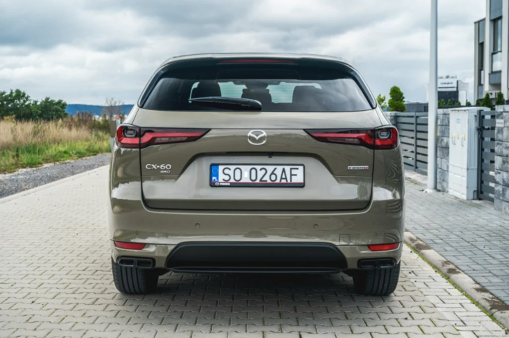 Mazda CX-60 Tylny widok beżowego samochodu osobowego marki Mazda CX-60 zaparkowanego na brukowanej drodze, z dobrze widoczną tablicą rejestracyjną i charakterystycznymi reflektorami LED.