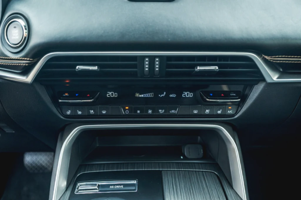 Mazda CX-60 Panel sterowania klimatyzacją i nawiewami w samochodzie, cyfrowy wyświetlacz temperatury po stronie kierowcy i pasażera, przyciski do ustawienia intensywności nawiewu, podgrzewania szyb oraz innych funkcji komfortu, eleganckie wykończenie konsoli centr...
