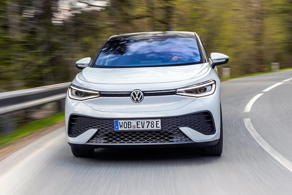 Co czwarty sprzedawany w Niemczech elektryk rejestrowany jest przez dealera. To sposób na uniknięcie kar za emisję CO2 Elektryczny samochód Volkswagen ID.4 jadący po krętej szosie w otoczeniu zieleni i rozmazanego tła, widoczny z przodu, z wyraźnym logo marki na masce.