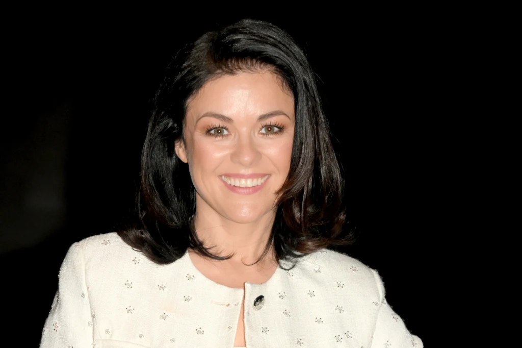 Katarzyna Cichopek dobrze czuje się w futerkach i kożuszkach. Ma ich całkiem sporo Młoda kobieta z ciemnymi włosami i jasną cerą uśmiecha się do obiektywu, ubrana w jasną marynarkę z drobnym wzorem, znajduje się na ciemnym tle.