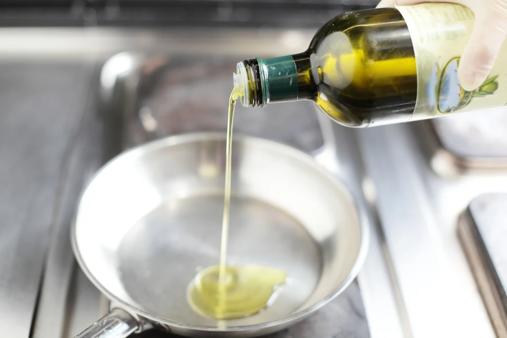 Wlewanie oliwy z butelki do czystej, metalowej patelni podczas przygotowań do smażenia.