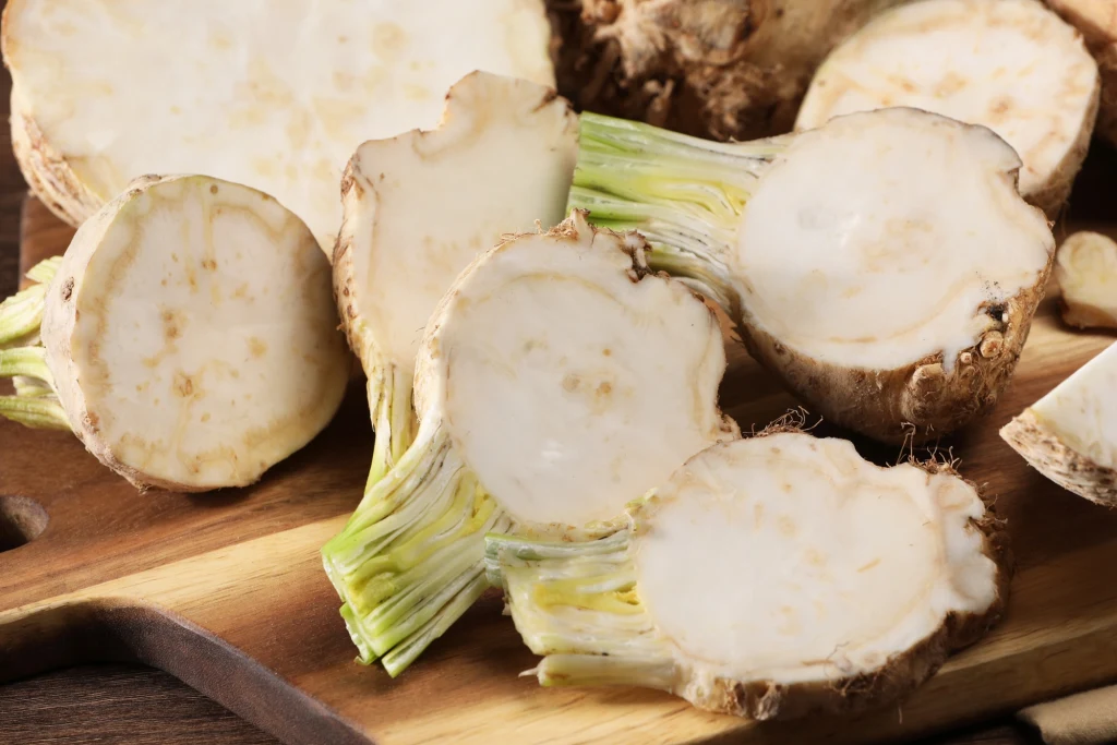 Seler korzeniowy zazwyczaj odgrywa poboczną rolę w polskiej kuchni, a szkoda Kilka pokrojonych bulw selera na drewnianej desce, wyraźnie widoczne białe wnętrze z żółto-zielonym przejściem do łodyg.