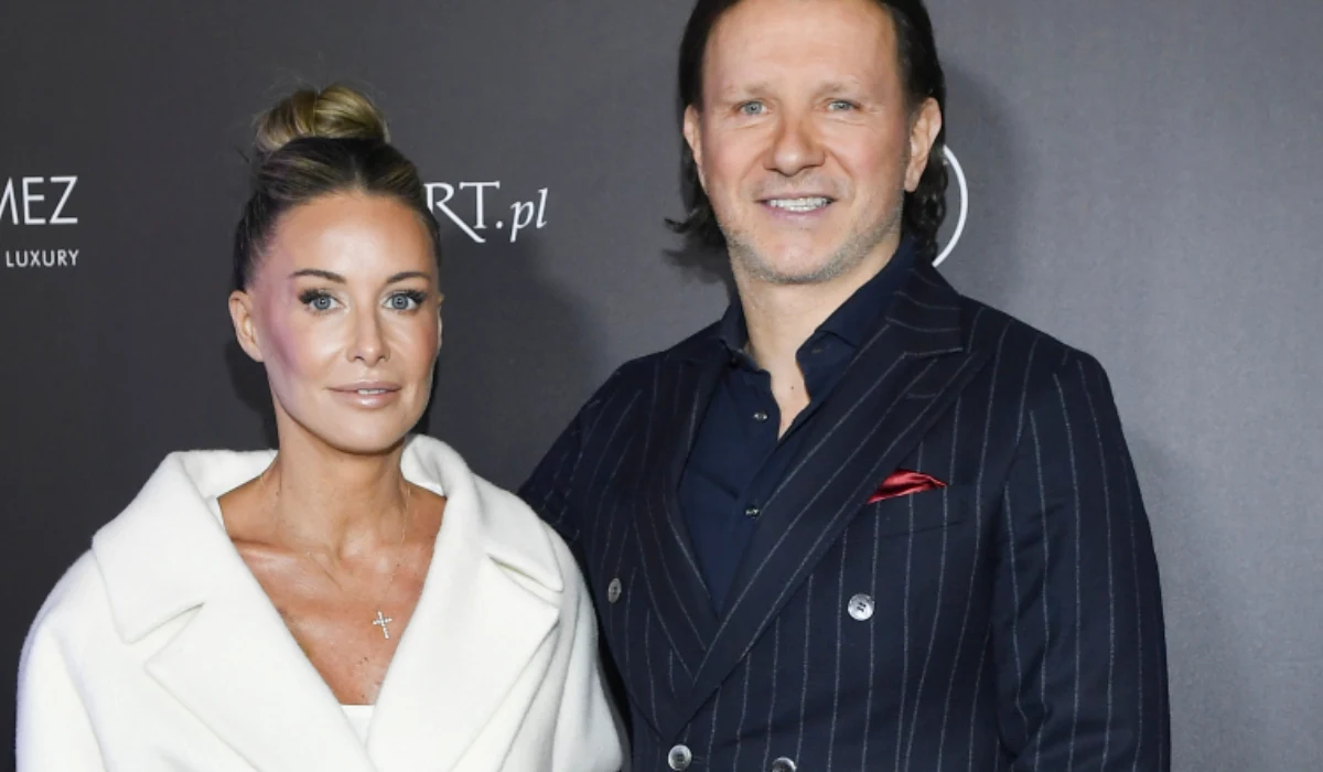 Małgorzata Rozenek-Majdan, Radosław Majdan Kobieta w białym płaszczu oraz mężczyzna w ciemnym garniturze w prążki stoją razem na tle ciemnej ścianki z logo, oboje uśmiechnięci.