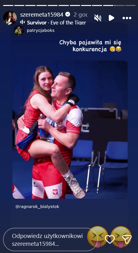 Mężczyzna w sportowym stroju trzyma na rękach uśmiechniętą kobietę również w stroju sportowym, oboje wyglądają na szczęśliwych, w tle niebieskie ściany i kilka krzeseł.