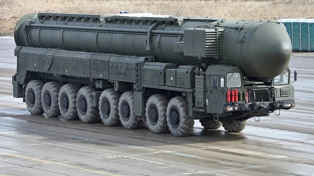 Wielka katastrofa superbroni Władimira Putina. Awangard eksplodował Ciężki wojskowy pojazd wielokołowy z dużą wyrzutnią pocisków międzykontynentalnych na asfaltowej powierzchni, otoczony surowym, polnym krajobrazem.