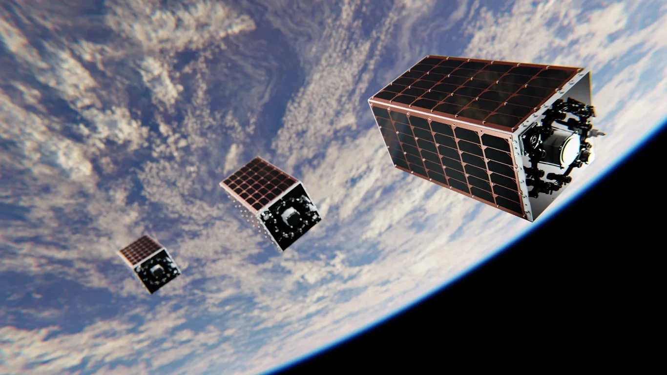 Polskie satelity ICEYE i PIAST poleciały na orbitę Trzy małe satelity w kształcie sześcianu unoszą się nad powierzchnią Ziemi, w tle widoczne chmury i zakrzywiony horyzont planety.