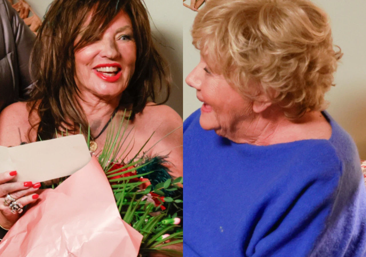 Agnieszka Fitkau-Perepeczko, Teresa Lipowska Dwie starsze kobiety w towarzyskiej rozmowie, jedna z nich trzyma bukiet kwiatów owinięty różowym papierem i kartkę, druga ubrana w niebieski sweter zwraca się do niej z uśmiechem.