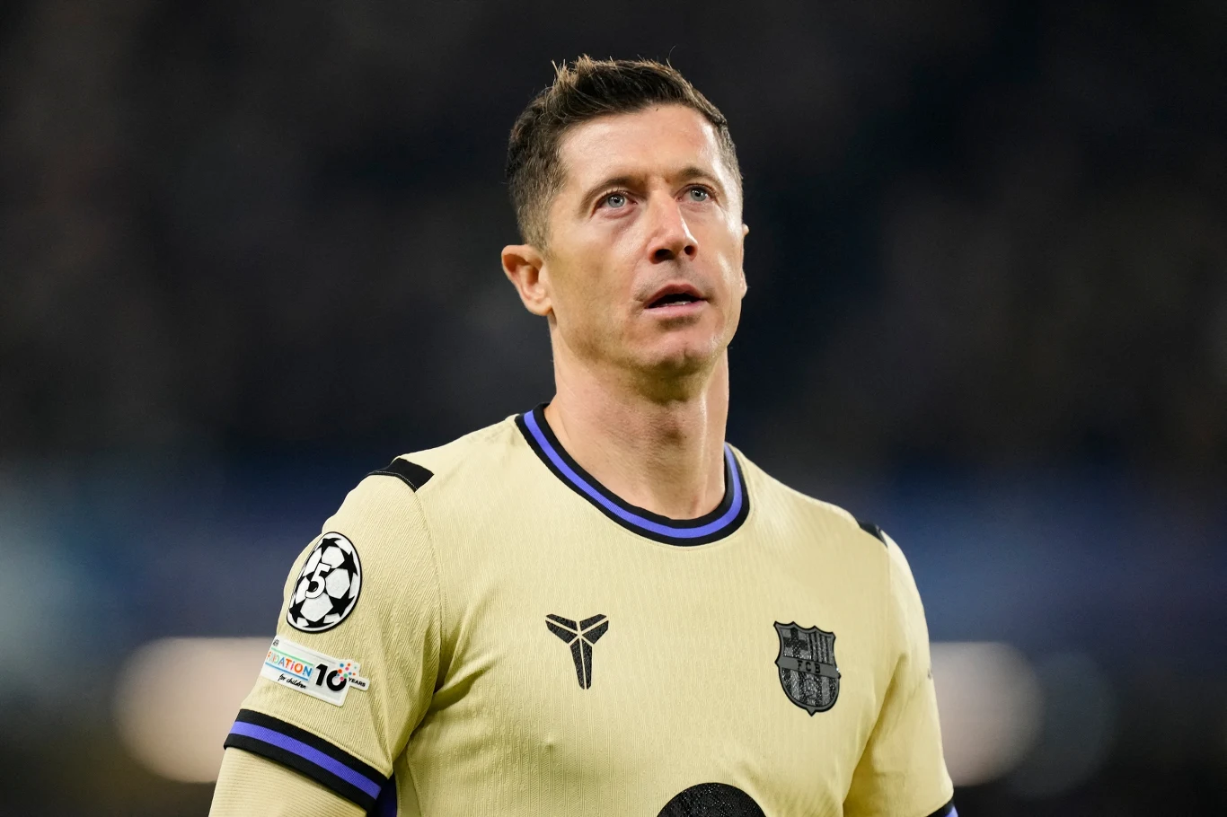 Piłkarz w jasnej koszulce z herbem FC Barcelona, patrzący przed siebie na boisku podczas meczu, na ramieniu opaska z logo Ligi Mistrzów