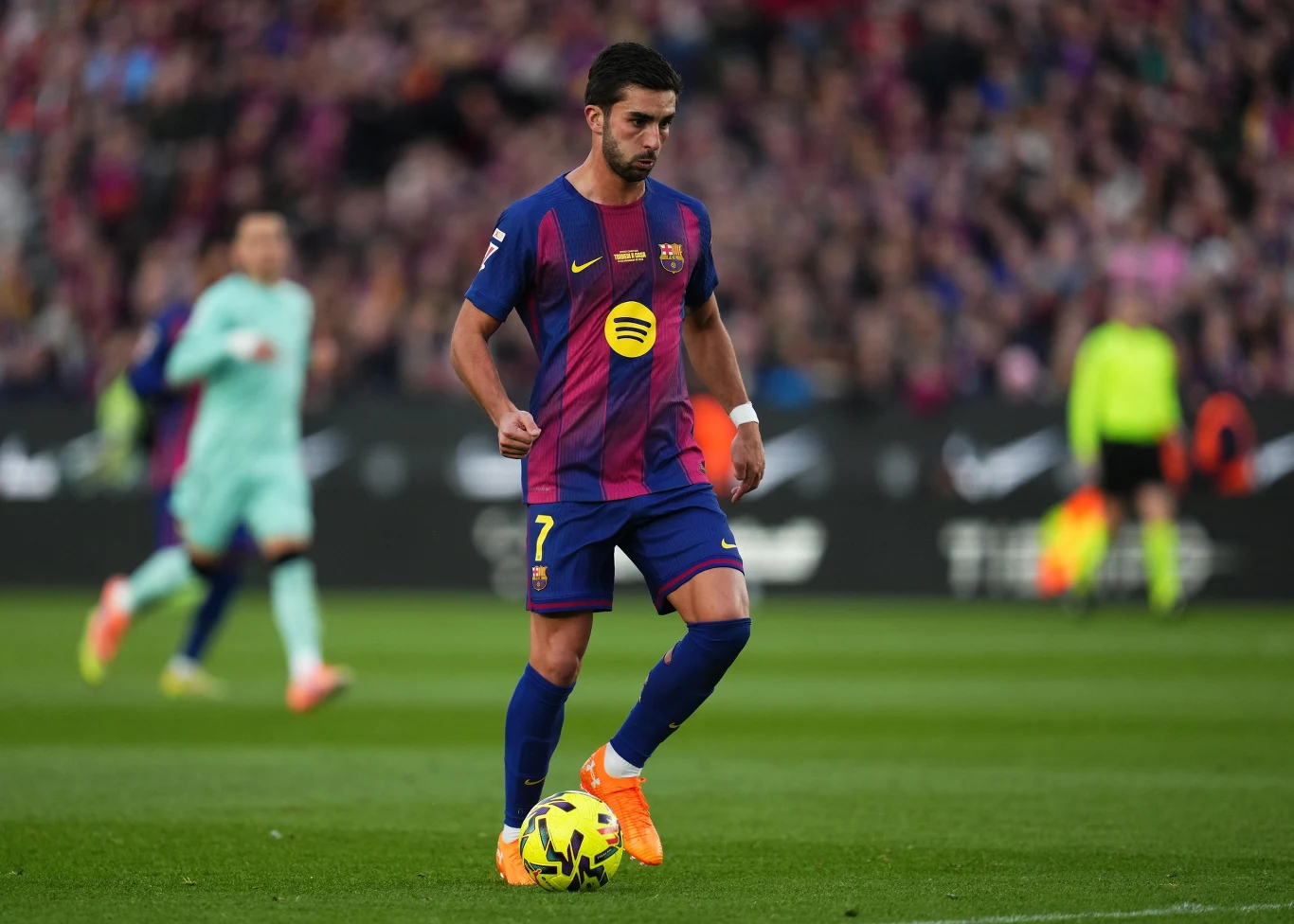 Zawodnik drużyny FC Barcelona w stroju meczowym kontroluje piłkę na boisku podczas meczu piłki nożnej, w tle widoczni są inni gracze oraz tłum kibiców na trybunach.