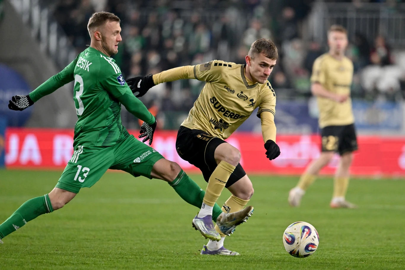 Jan Grzesik (z lewej) kontra Matusz Kmet. Piłkarze Radomiaka podjęli lidera tabeli bez cienia kompleksów Dwóch piłkarzy rywalizuje o piłkę podczas meczu piłki nożnej na stadionie, w tle rozmyci zawodnicy i kibice.