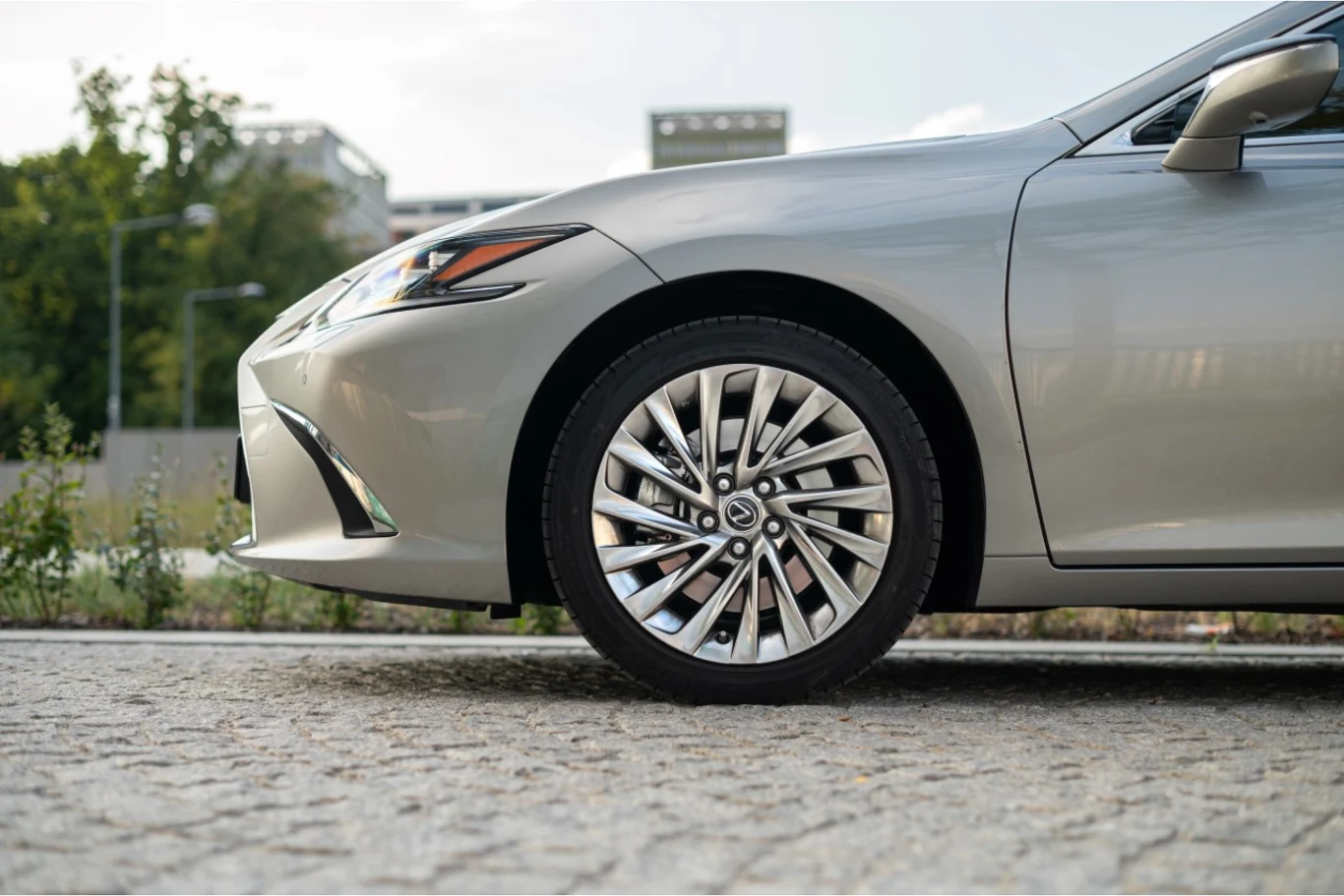 W 5 lat przejechał bezawaryjnie ponad 750 tys. km. Przednia część srebrnego samochodu osobowego z wyeksponowanym dużym aluminiowym kołem i oponą, zaparkowana na brukowanej nawierzchni, w tle zieleń i fragment nowoczesnego budynku.