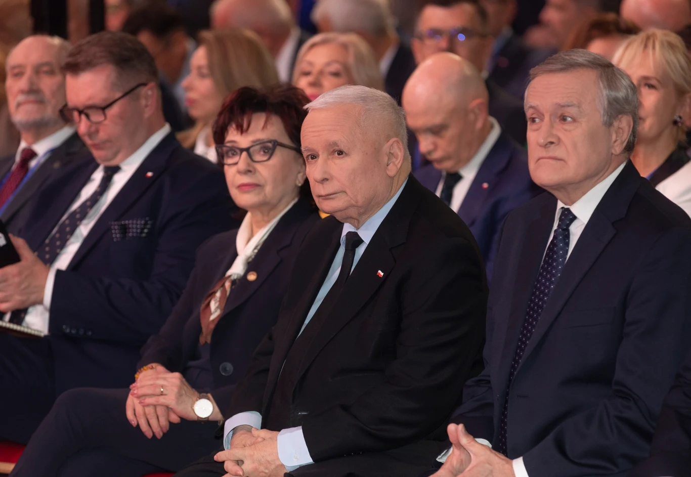 Sondaż: Czy PiS wróci do władzy w 2027 roku? (zdj. ilustracyjne) Grupa elegancko ubranych osób siedzi w pierwszym rzędzie podczas oficjalnego wydarzenia, ich wyraz twarzy jest skupiony i poważny, w tle znajdują się inni uczestnicy uroczystości.