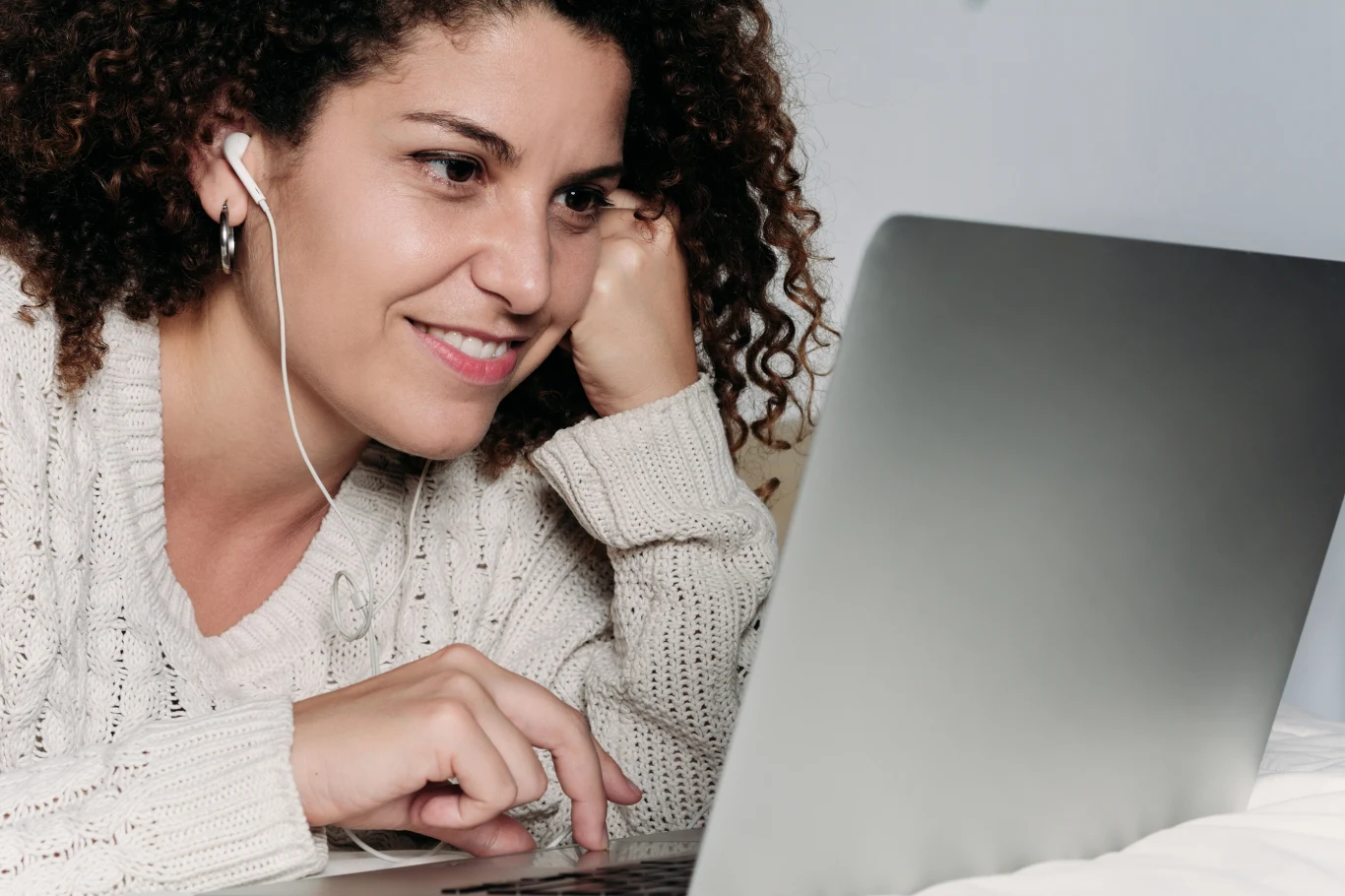 Sprawdź, czy jesteś prawdziwym introwertykiem. Dziewięć nietypowych cech Kobieta z kręconymi włosami uśmiecha się, leżąc na łóżku i słuchając czegoś przez słuchawki podłączone do laptopa. Ubrana jest w jasny sweter, skupiona na ekranie komputera.