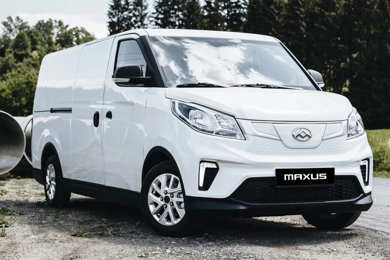 Rozwój chińskiej elektromobilności w segmencie aut dostawczych zagraża europejskim producentom. Na zdjęciu Maxus e-Deliver 3 Biały samochód dostawczy marki Maxus zaparkowany na żwirowym placu, w tle widoczne drzewa i fragment betonowych rur.