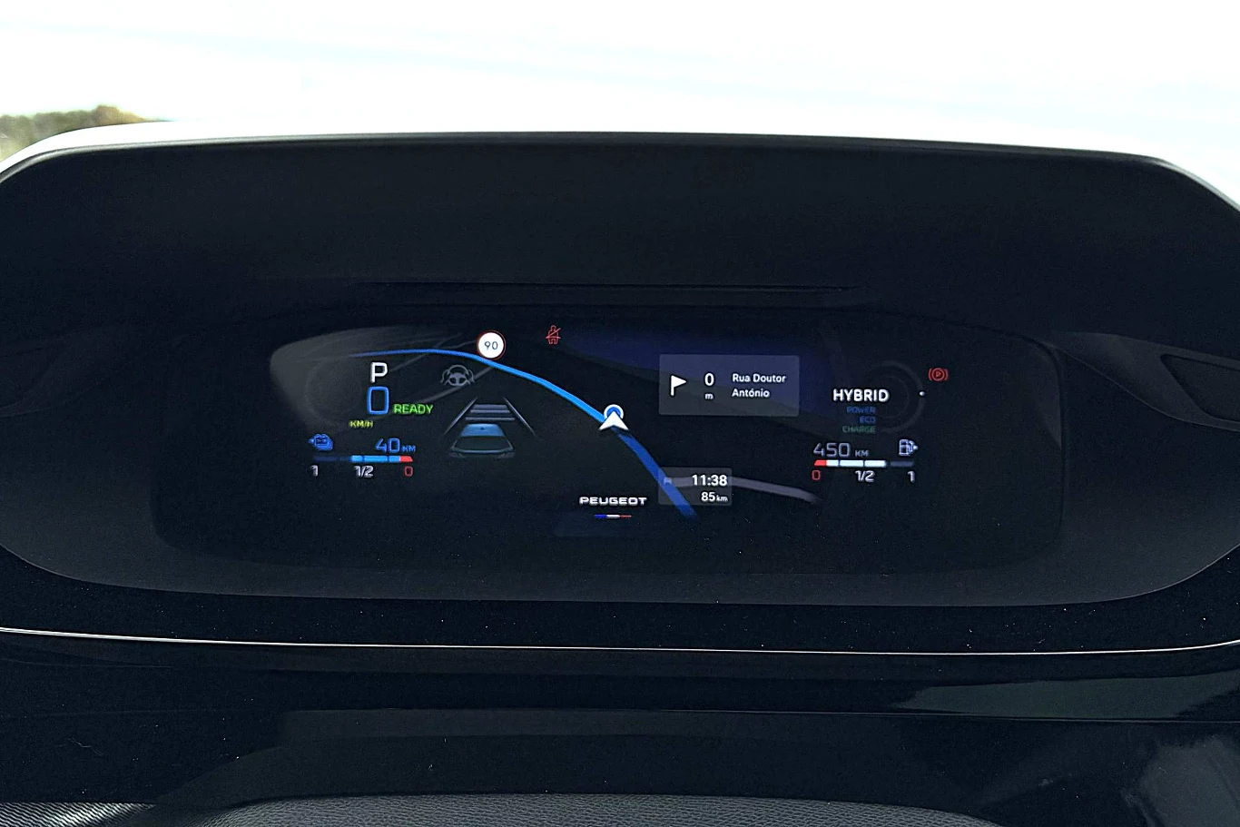 Nowa grafika wyświetlacza wskaźników w zmodernizowanym Peugeocie 308. Cyfrowy kokpit samochodowy prezentuje prędkościomierz, wskaźnik ładowania baterii, tryb jazdy oraz system nawigacyjny aktywny na wyświetlaczu. Logo Peugeot widoczne pośrodku panelu.