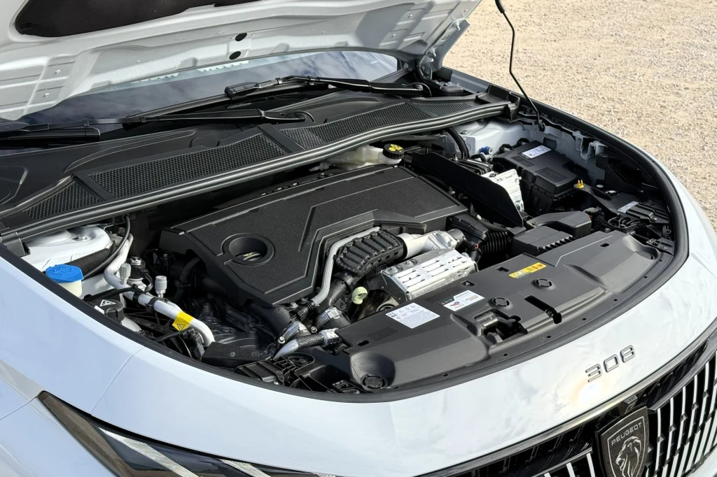 Silnik samochodowy w białym samochodzie marki Peugeot 308, widoczna komora silnika z rozmaitymi elementami technicznymi i pokrywą silnika.