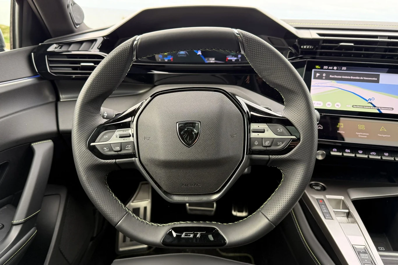 Nowoczesna kierownica samochodowa z logotypem producenta pośrodku, liczne przyciski do sterowania multimediów oraz wyświetlacz na desce rozdzielczej ze wskaźnikami i ekranem nawigacji.