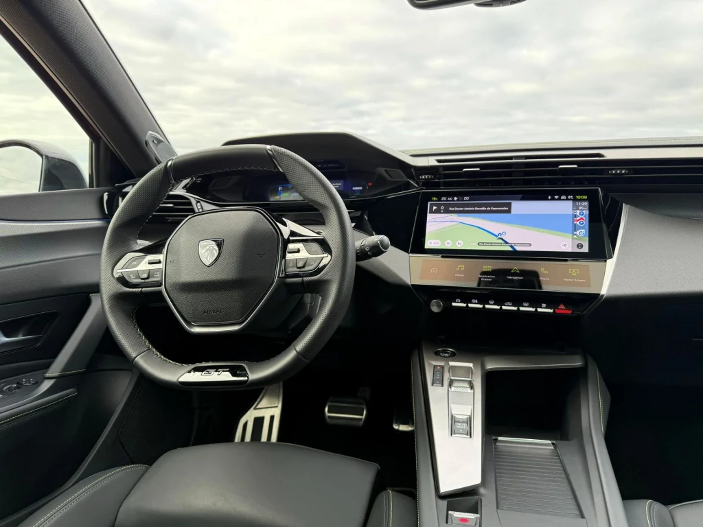 Nowoczesne wnętrze samochodu z cyfrowym kokpitem, kierownicą wielofunkcyjną, dużym ekranem dotykowym z nawigacją oraz konsolą środkową z przyciskami i dźwignią zmiany biegów