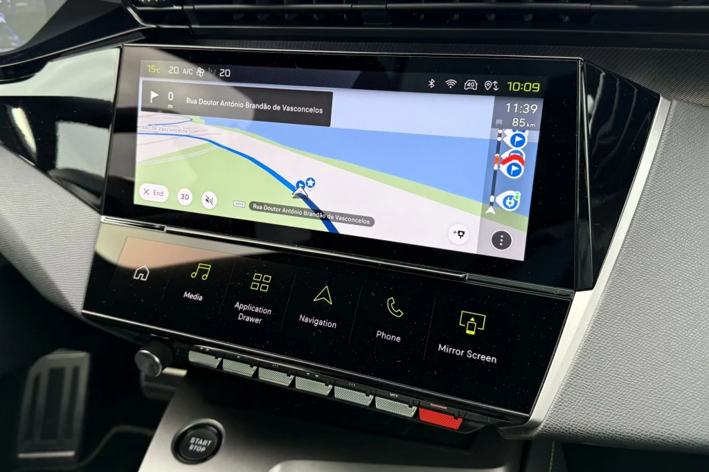 Nowoczesny ekran dotykowy w samochodzie z uruchomioną nawigacją, pokazujący mapę, informacje o trasie oraz ikonki aplikacji takich jak media, telefon czy ustawienia pojazdu. Panel z przyciskami funkcyjnymi i przyciskiem startu silnika znajduje się poni...