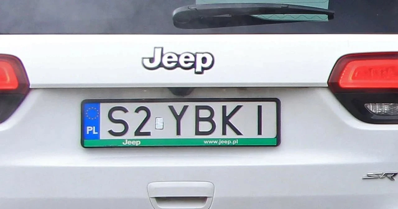 Dzięki specjalnemu formularzowi w kilka minut sprawdzisz dostępność wybranej przez siebie indywidualnej tablicy rejestracyjnej Tył białego samochodu Jeep z polską tablicą rejestracyjną S2 YBKI, w tle widoczne tylne światła oraz wycieraczka szyby.