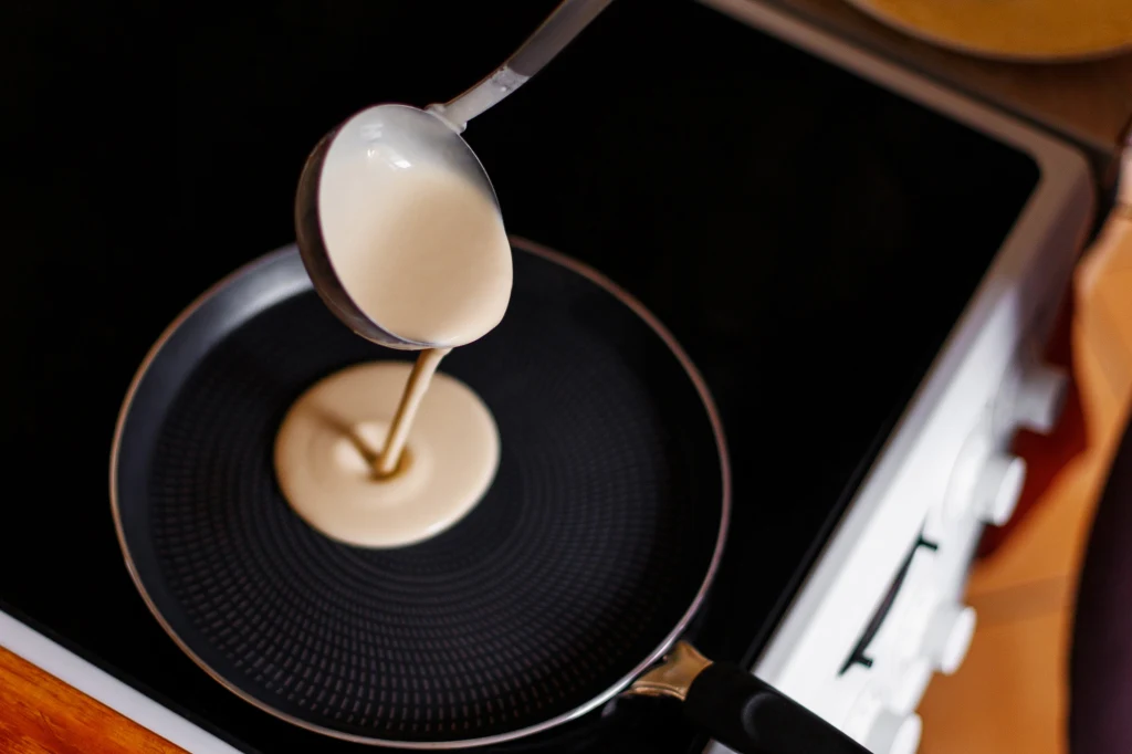 Naukowcy opracowali skuteczną metodę recyklingu teflonu Porcja ciasta naleśnikowego wylewana chochlą na rozgrzaną patelnię znajdującą się na kuchence.