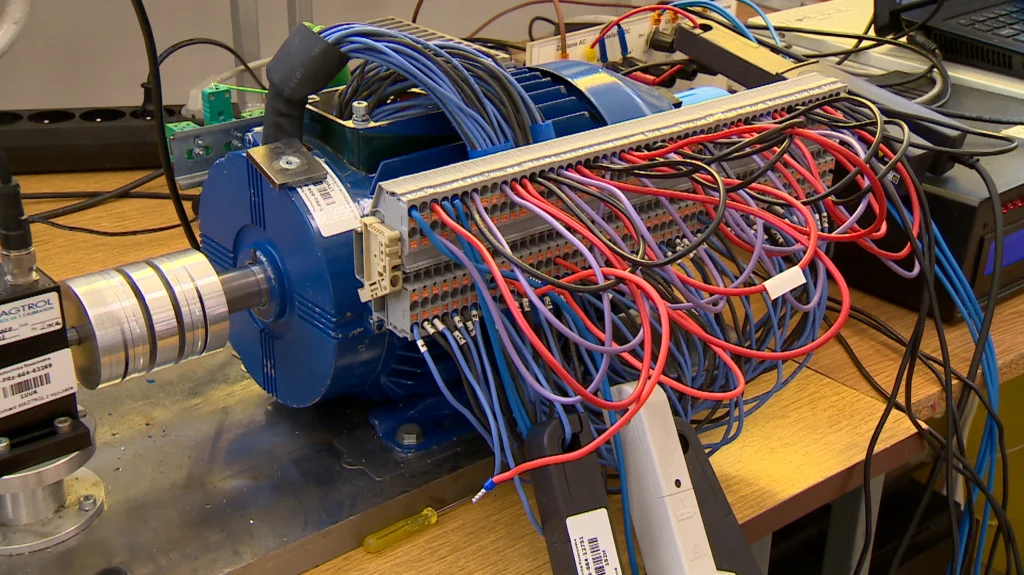 Silnik elektryczny z licznymi kolorowymi przewodami podłączonymi do listwy zaciskowej, ustawiony na metalowym blacie roboczym w laboratorium elektrycznym.