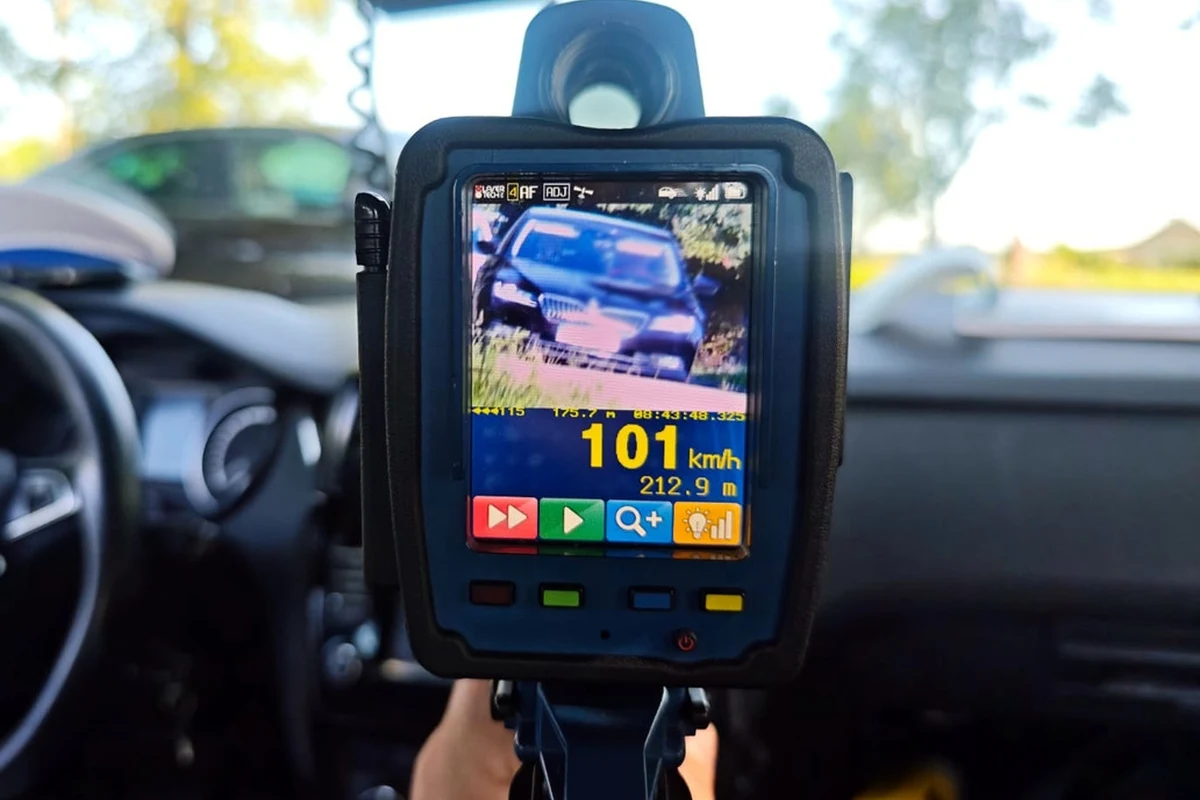 Kierowcy już wkrótce będą tracić prawo jazdy na trzy miesiące również w terenie niezabudowanym. Ręczny miernik prędkości rejestrujący samochód osobowy jadący z prędkością 101 km/h, wyświetlacz pokazuje odległość do pojazdu oraz dodatkowe informacje wizualne, wnętrze radiowozu w tle.