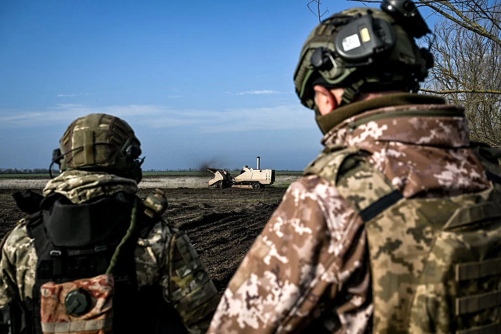 Ukraińscy żołnierze zdecydowanie komentują plan pokojowy Donalda Trumpa Dwóch żołnierzy w kamuflażu obserwuje poligon, po którym porusza się zdalnie sterowany pojazd wojskowy na tle bezchmurnego nieba.