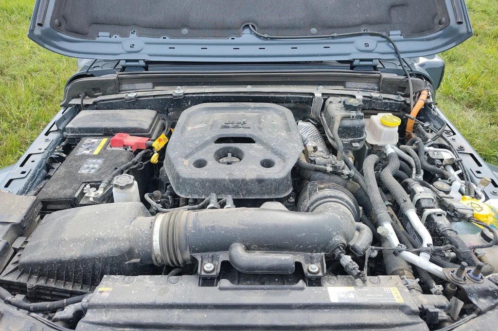 Moc systemowa hybrydowego napędu wynosi 380 KM Komora silnika samochodu terenowego z wyraźnie widocznym silnikiem Diesla, akumulatorem po lewej stronie oraz przewodami i elementami układu elektrycznego i chłodzenia. Obudowa filtra powietrza i złącza serwisowe są dobrze widoczne, całość pokryta cien...