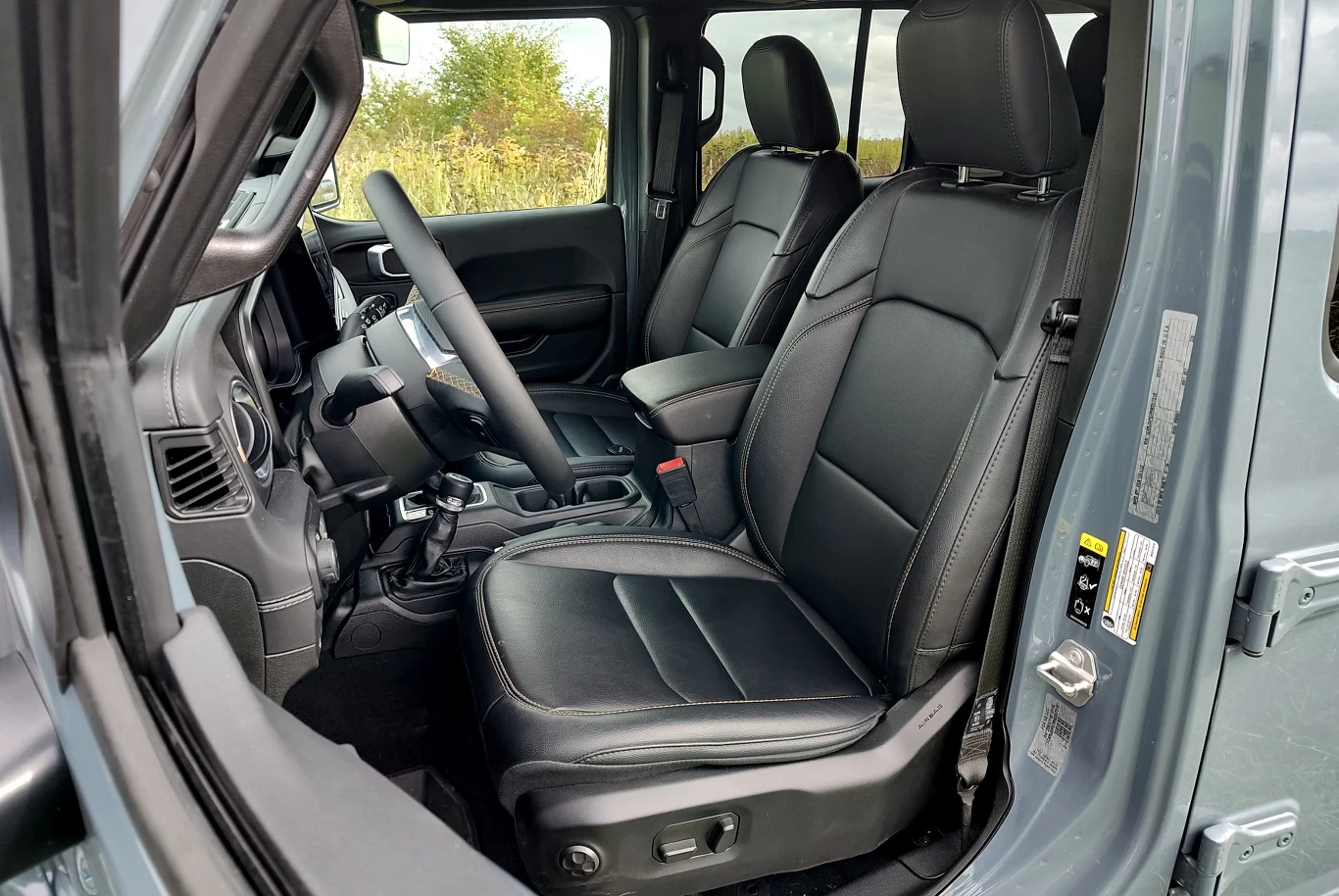 Jeep Wrangler Sahara Czarne, skórzane fotele w nowoczesnym samochodzie terenowym, szerokie drzwi otwarte, widoczne elementy kokpitu i konsoli środkowej, przestronne wnętrze z wysokiej jakości materiałów.