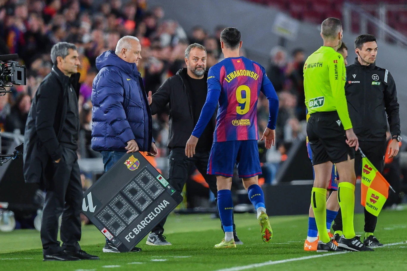 Zawodnik w koszulce z numerem 9 opuszcza boisko podczas zmiany, obok sędziowie oraz tablica elektroniczna z logo FC Barcelona, w tle widownia stadionu.