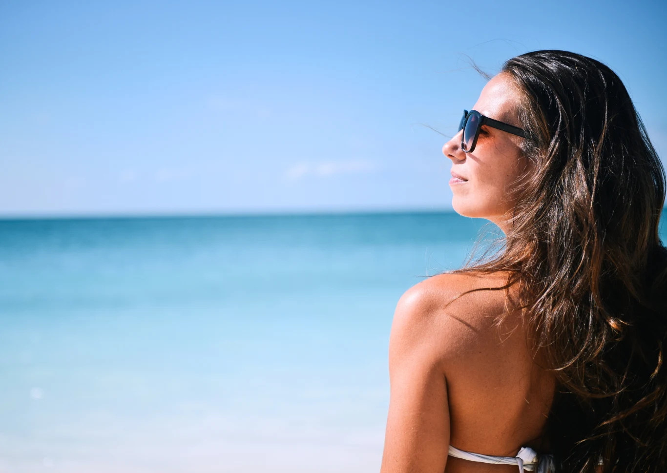 Turcja czy Grecja – gdzie na tańsze wakacje 2026? Plażowanie w słońcu nad turkusowym morzem Kobieta w okularach przeciwsłonecznych patrząca w stronę morza, błękitna woda i niebo w tle, letnia sceneria