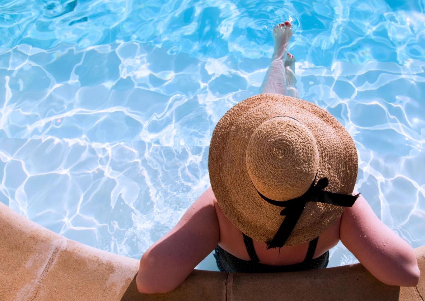 All Inclusive 2026 – porównanie Turcji i Grecji. Relaks przy basenie w wakacyjnym kurorcie Osoba w dużym słomkowym kapeluszu relaksuje się, siedząc na brzegu basenu z nogami zanurzonymi w krystalicznie czystej wodzie.