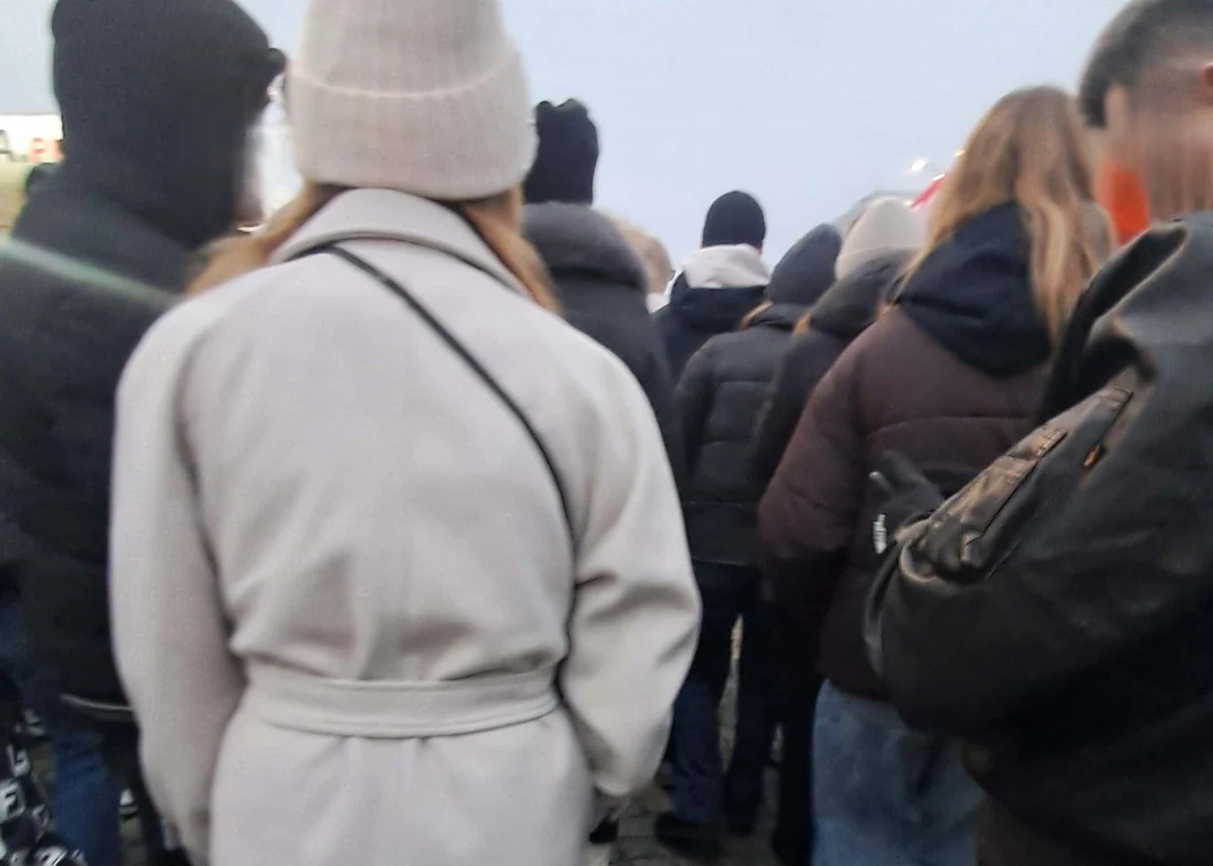 Idąc na jarmark bożonarodzeniowy w Warszawie trzeba się przygotować na to, że od początku do końca będzie się stało w długiej kolejce Tłum ludzi stojących blisko siebie, ubranych w zimowe kurtki i czapki, widocznych od tyłu podczas zgromadzenia na świeżym powietrzu.